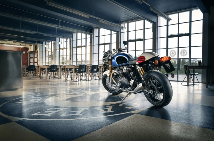 Motorcycle parked inside a high-ceilinged building with large windows, checkered flooring, and tables and chairs.