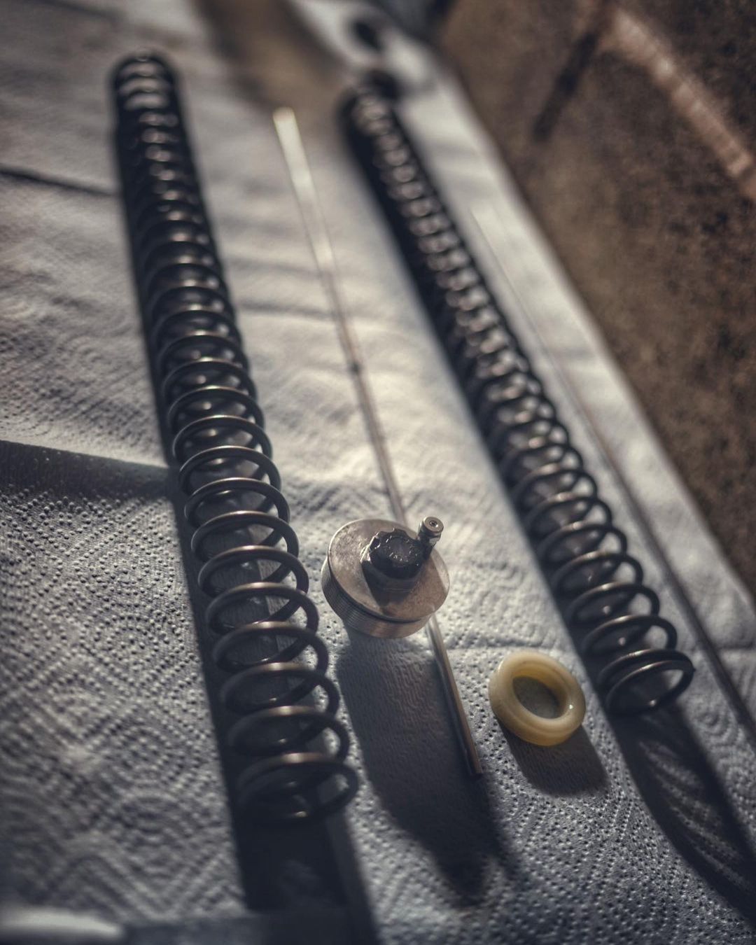 Close-up of disassembled metal springs, rod, and ring laid out on a textured surface, possibly for repair or maintenance in an industrial setting.