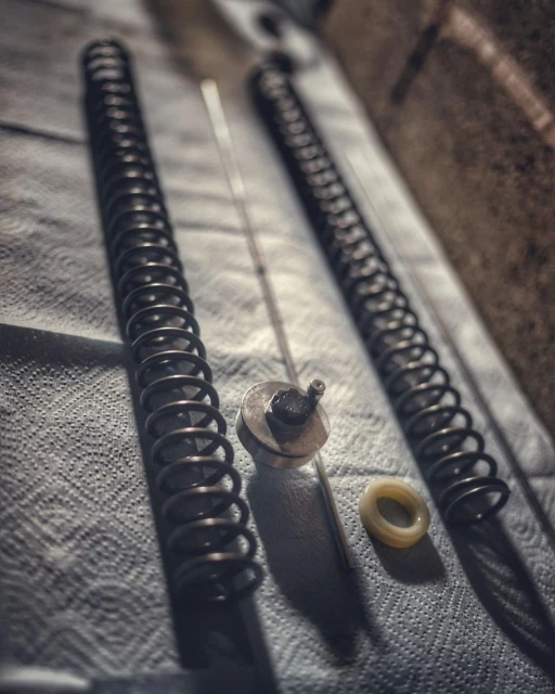 Close-up of disassembled metal springs, rod, and ring laid out on a textured surface, possibly for repair or maintenance in an industrial setting.