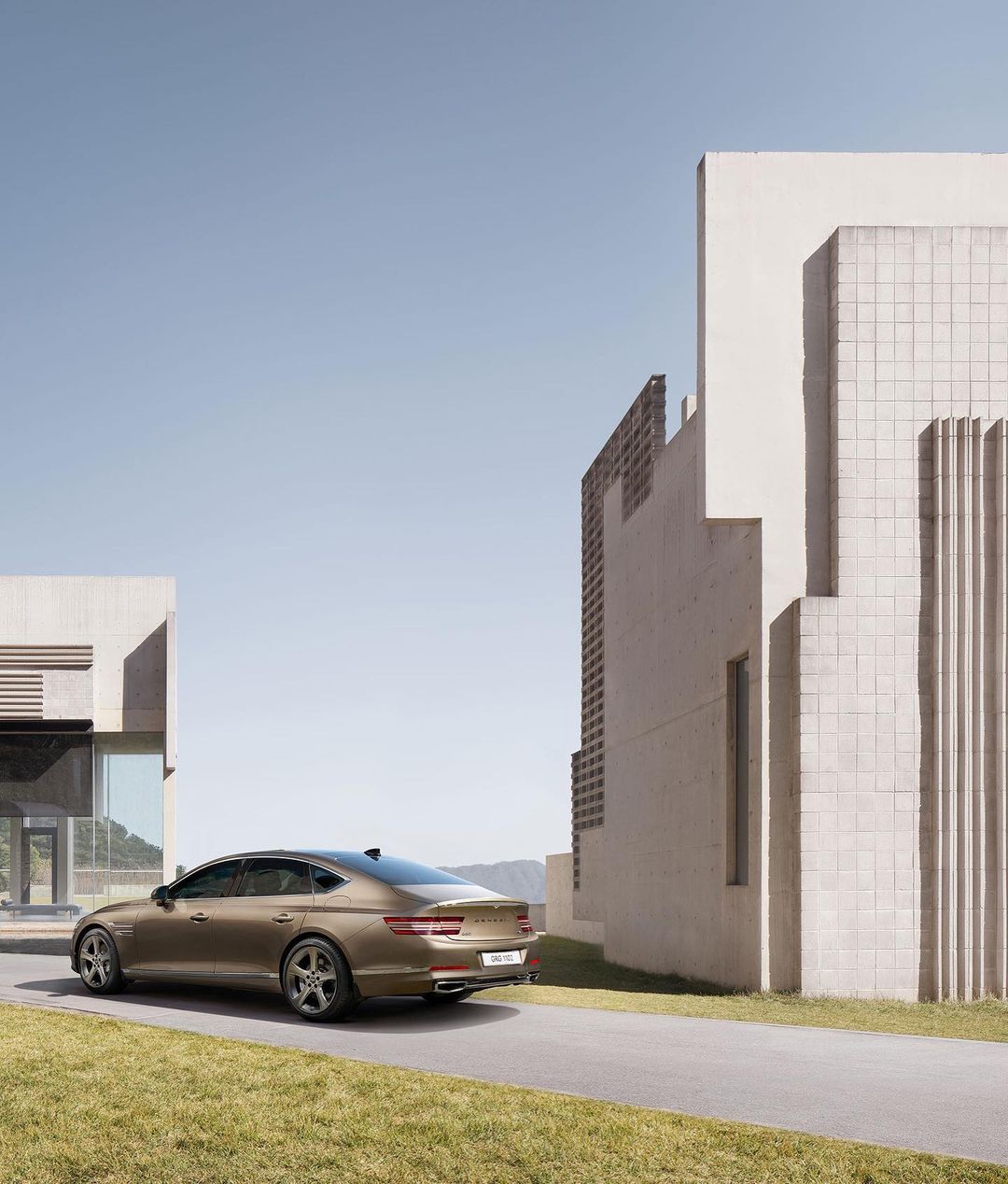 Bronze sedan parked on an asphalt driveway in front of a modern white building with grass and blue sky on a sunny day. Automotive.