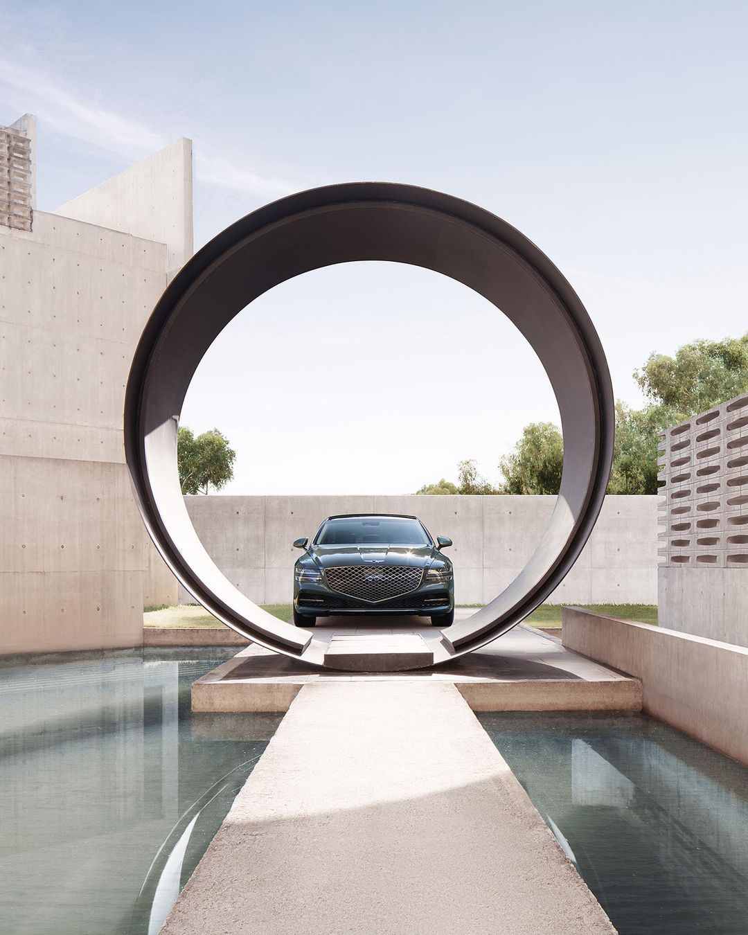 Green Genesis sedan showcased in a minimalist architectural setting, reflected in water, emphasizing design and luxury.