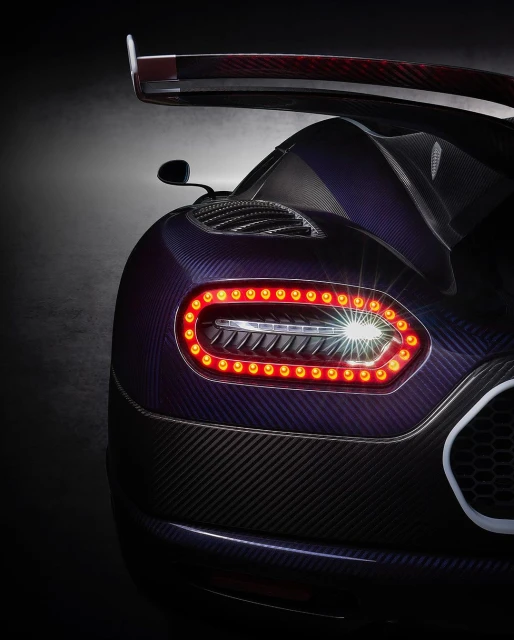 Close-up of the rear of a dark purple and black Koenigsegg Jesko showcasing its taillights, carbon fiber texture, and rear wing design.