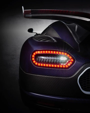 Close-up of the rear of a dark purple and black Koenigsegg Jesko showcasing its taillights, carbon fiber texture, and rear wing design.