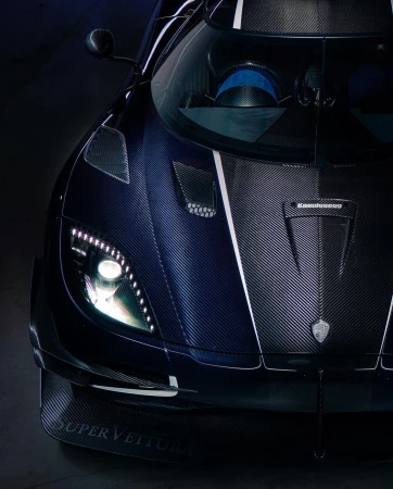 Close-up of a dark blue Koenigsegg sports car showing the front headlights, hood, and carbon fiber texture, conveying luxury and high performance.