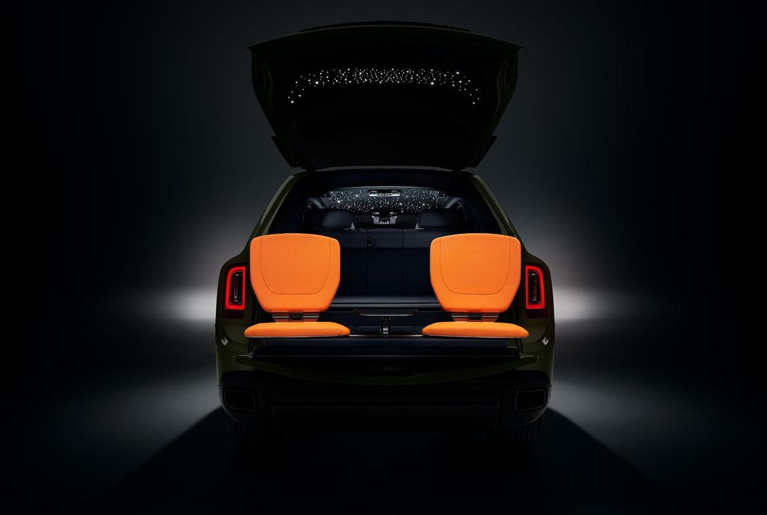 Luxury SUV with open trunk and rear seating, showcasing orange leather seats and star light ceiling in a dark interior.