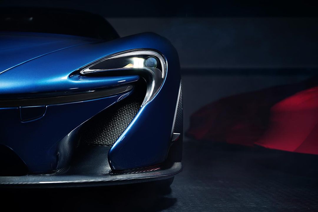 Close-up of a shiny blue McLaren sports car showing the sleek design and headlight detailing against a dark background in a studio.