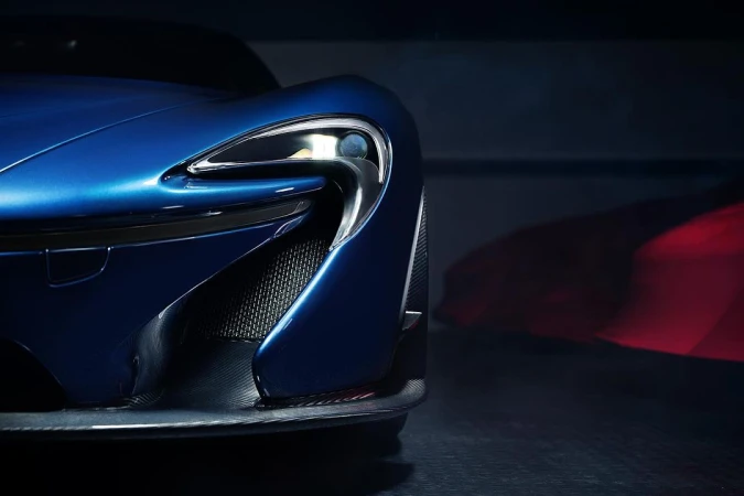 Close-up of a shiny blue McLaren sports car showing the sleek design and headlight detailing against a dark background in a studio.