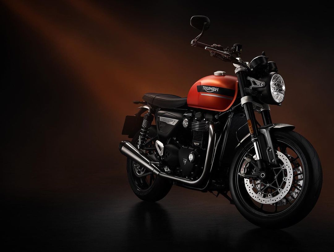 Triumph Speed Twin 900 motorcycle on display, featuring a combination of orange and black colors, sleek design, and studio lighting.