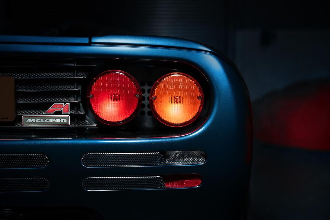 Close-up of the rear of a blue McLaren F1 supercar with its iconic taillights illuminated, highlighting its design and automotive craftsmanship.