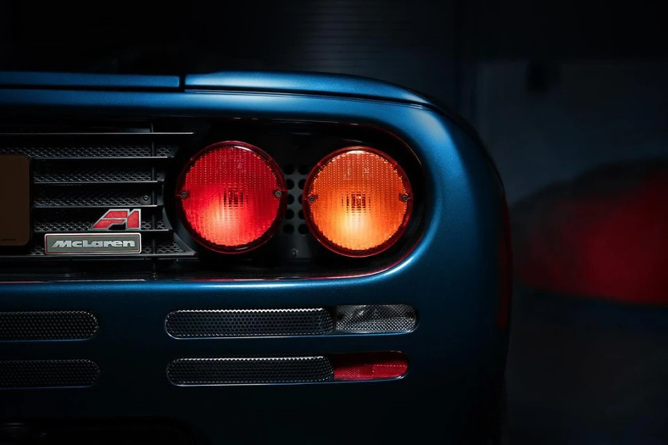 Close-up of the rear of a blue McLaren F1 supercar with its iconic taillights illuminated, highlighting its design and automotive craftsmanship.