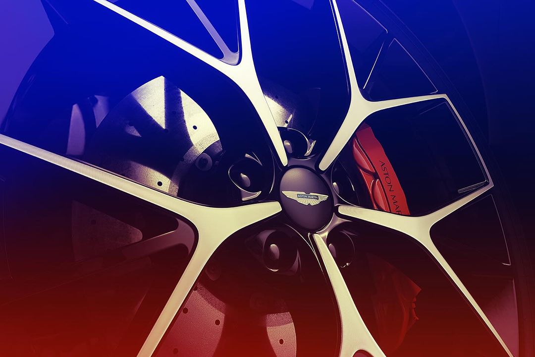 Close-up of an Aston Martin car wheel featuring a black rim, multi-spoke design with silver accents, and a red brake caliper.