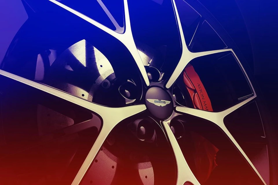 Close-up of an Aston Martin car wheel featuring a black rim, multi-spoke design with silver accents, and a red brake caliper.