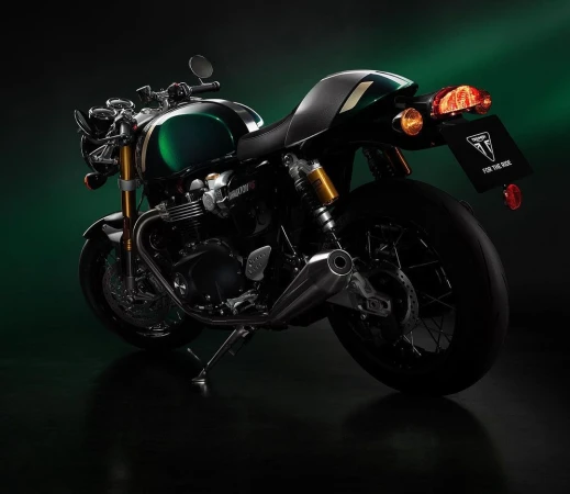 Rear view of a Triumph Thruxton RS motorcycle featuring a dark green fuel tank, black seat, and visible taillight on a dark background.