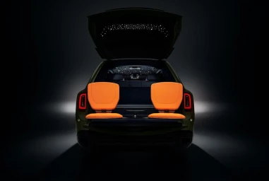 Rear view of luxury SUV with open tailgate and bright orange folding seats, illuminated ceiling stars, and dark studio background