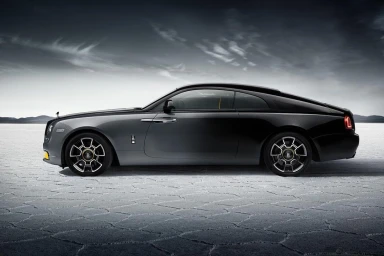Profile view of a luxury dark grey coupe car parked on a dry cracked salt flat under a dramatic cloudy sky