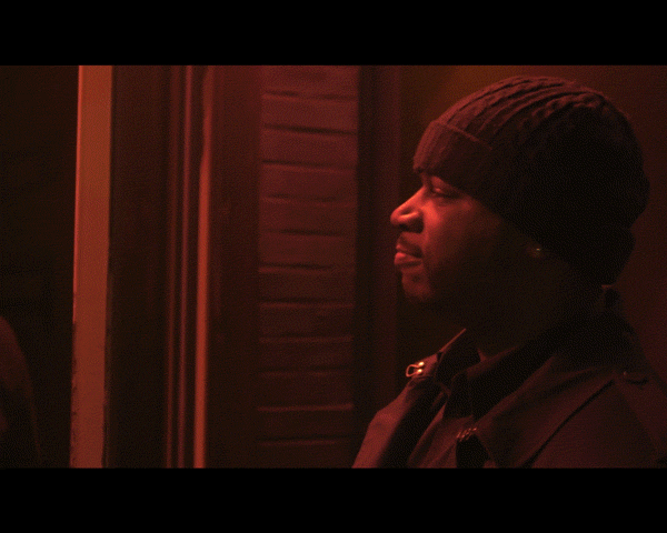 Adult male wearing beanie in profile with serious expression, monochrome red lighting, indoors.