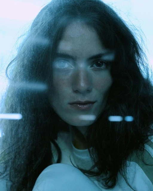 Portrait of a young adult woman with long dark hair and fair skin looking directly at the camera with a serious expression.