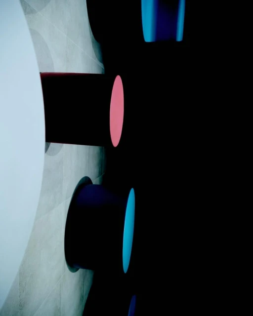 Abstract architectural detail featuring cylindrical shapes against a tiled wall and dark background, highlighted with vibrant pink and blue accents.
