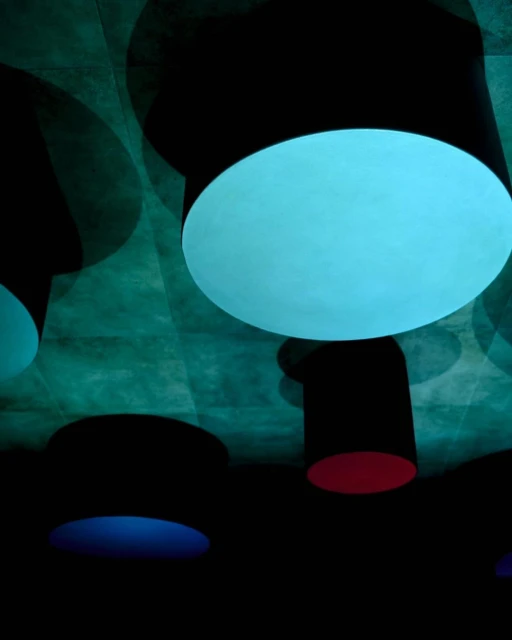 Abstract view of round, multicolored illuminated architectural lighting fixtures, suspended from a teal textured ceiling, creating a modern design.