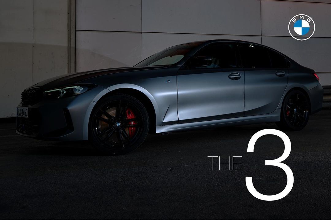 Gray BMW 3 Series sedan parked in an indoor setting with a dark gray surface and a geometric light gray wall in the background.