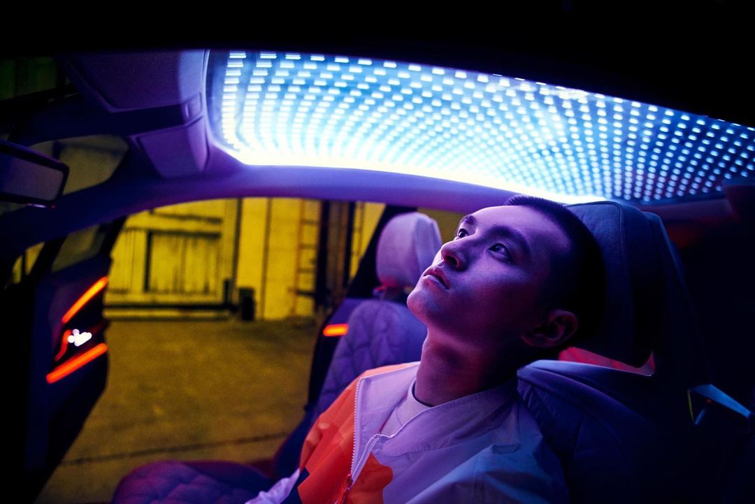 Young man gazes up inside a modern car interior with futuristic lighting. The scene is lit with neon blue and orange accents.