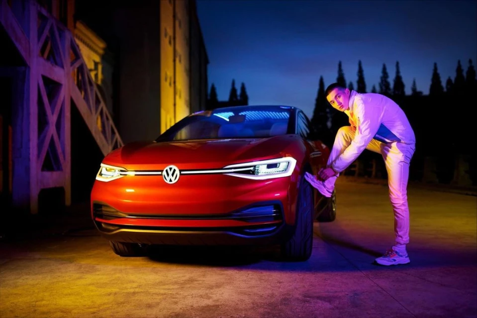 Red Volkswagen electric car with a man tying his shoe in an urban setting, lit with dramatic neon lights against a dark background.