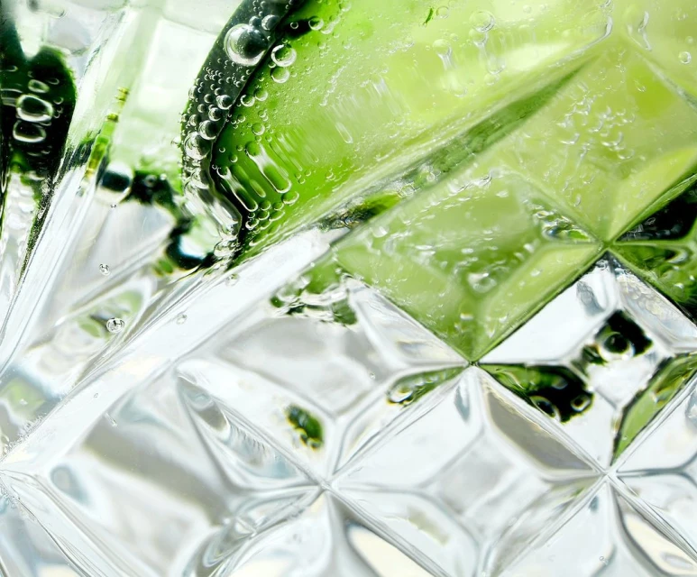 Close-up of a clear, patterned glass filled with water, lime slices, and bubbles, showcasing a refreshing drink.