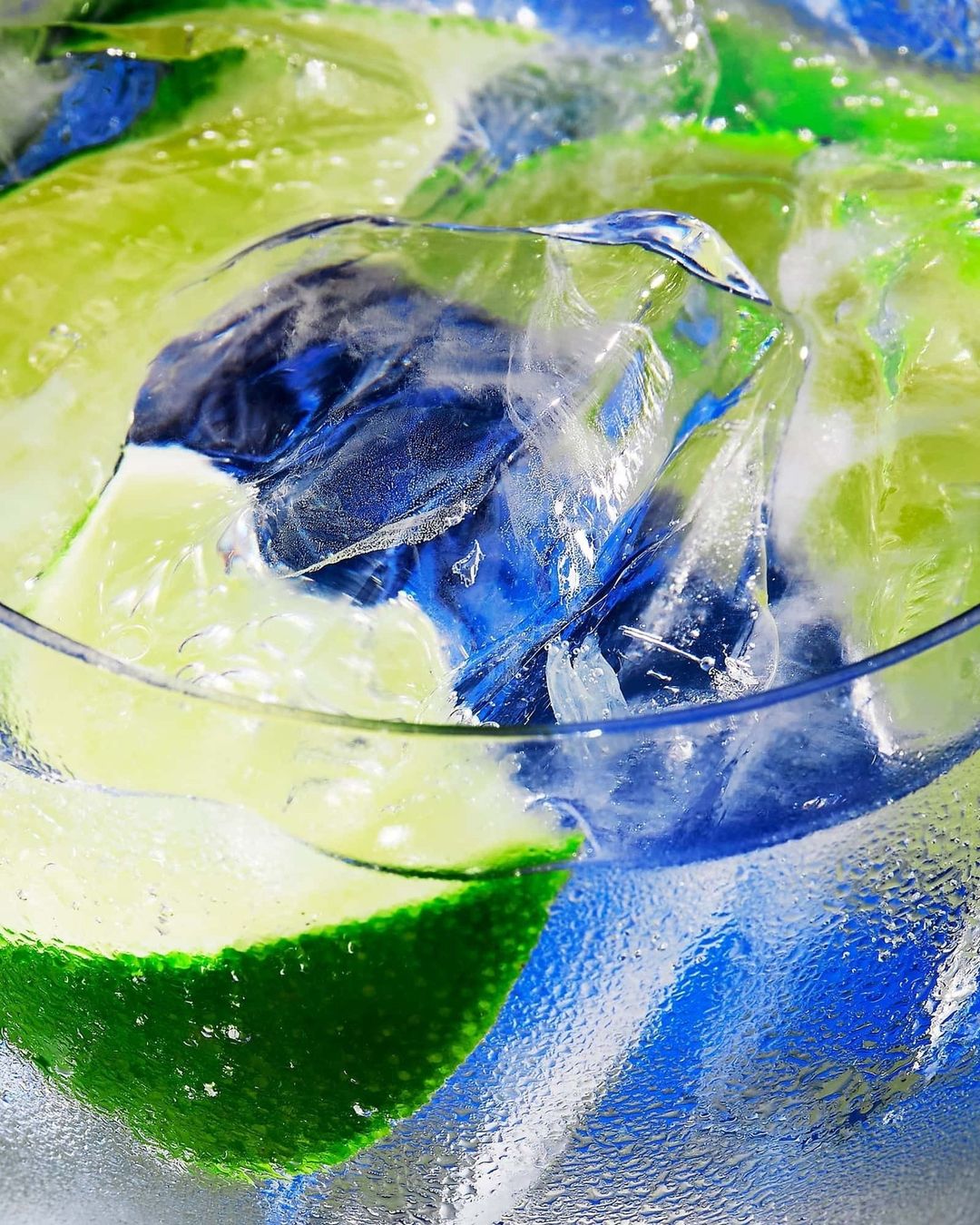 Close-up of a clear glass filled with clear ice cubes, lime slices, and condensation droplets covering the exterior.