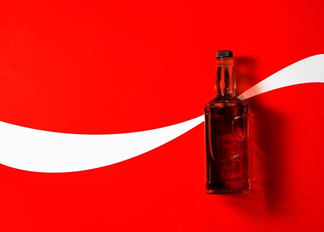 Liquor bottle in a glass container placed on a vibrant red background bisected by a white swoosh, creating a stark contrast.