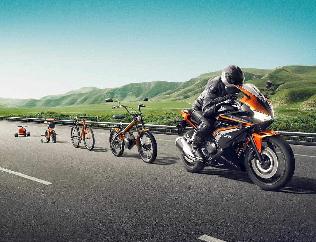 Motorcycle rider on road with evolution of bicycles, mountains and sky background. Man wearing helmet and protective gear, driving orange and black bike.