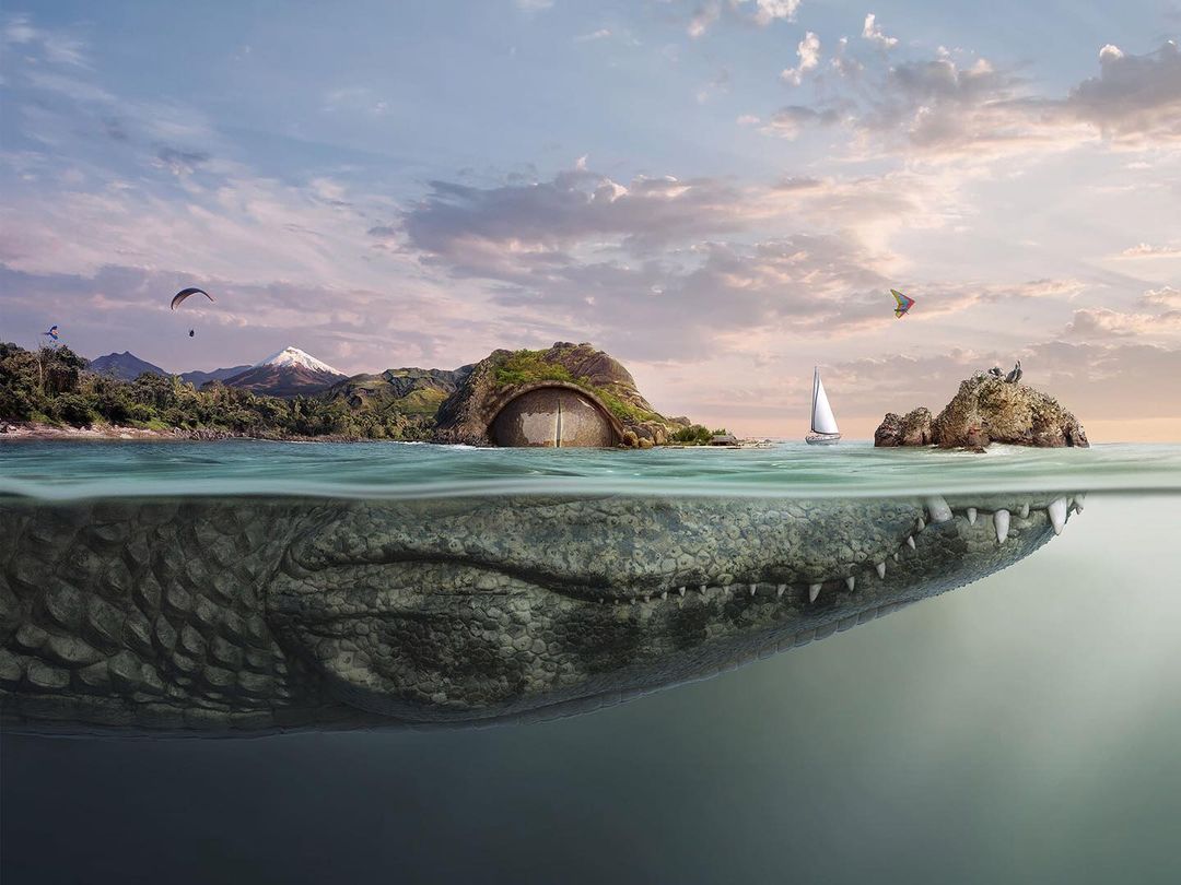 Surreal digital artwork features a submerged crocodile head below calm water with tropical islands, a sailboat, and parasailers.