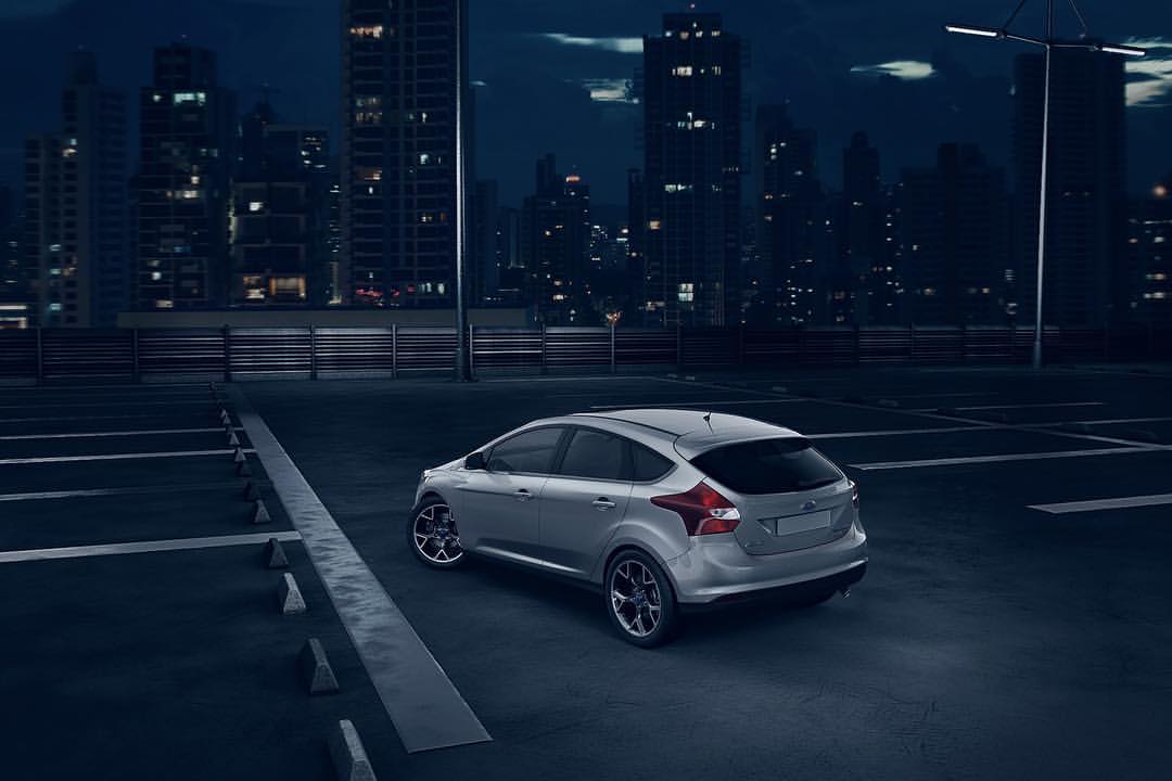 Silver Ford Focus parked on a rooftop at night, with city buildings illuminated in the background under a dark sky and streetlights.
