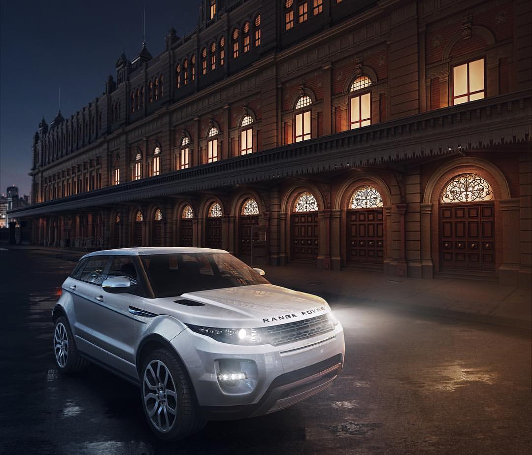 Silver Range Rover SUV parked on a street with a large brick building in the background at night, showcasing automotive design.