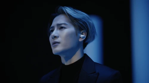 Portrait of a man with silver hair wearing a dark suit in cool-toned studio lighting, showcasing beauty and fashion with a modern edge.