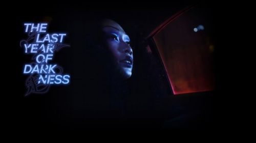 A woman's portrait with creative lighting, set against a dark background with prominent neon signage that reads 'The Last Year of Darkness'.