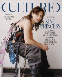 Magazine cover portrait of artist King Princess sitting on a stool wearing a patchwork tie top and dark trousers by photographer Angalis Field.