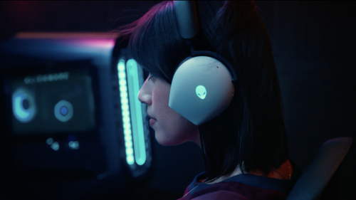 Profile view of a young adult with headphones and illuminated screen, highlighting a gaming or technology setup in a dim environment.