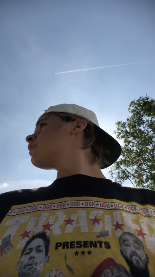 Teen male wearing a baseball cap and DGK t-shirt. He's photographed from a low angle against a bright blue sky and green tree.
