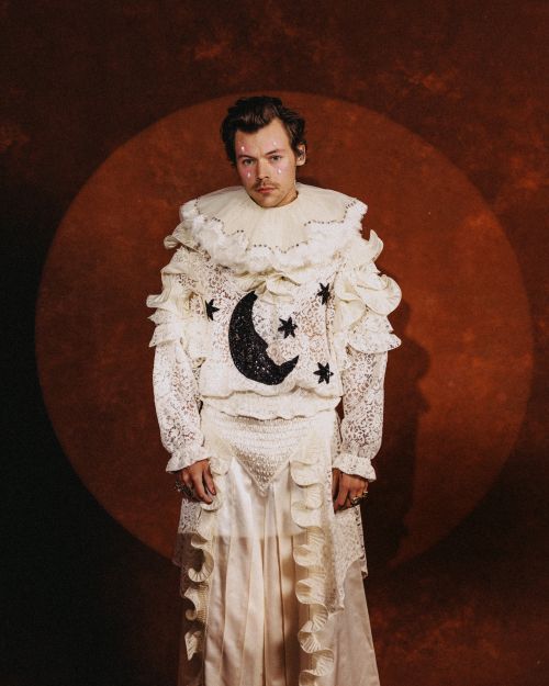 Adult male with light skin and brown hair poses wearing frilly white lace outfit with moon and star accents in photo studio.
