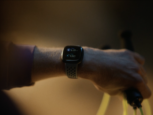 Close-up of a person's arm wearing a smartwatch showing fitness data while holding a black jump rope, captured in dim, warm light.