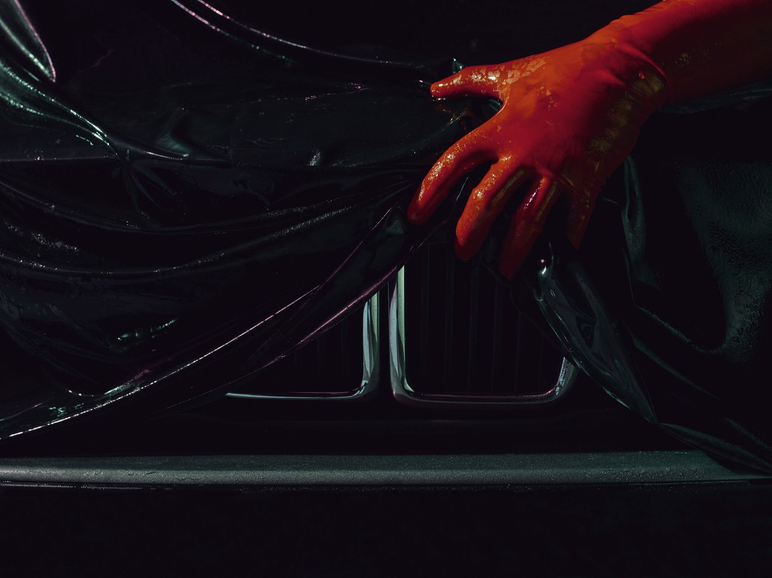 Close-up of a car hood with a protective black film being applied by a hand in a red glove, automotive industry, dramatic lighting.