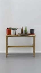 Wooden work table holding glass bottles, a metal paint can, a red plastic fuel container, and a small bucket against a white wall.