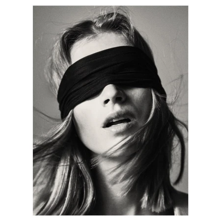 Monochrome portrait of a woman with a black blindfold, fair skin, and light hair. Studio shot with diffused lighting.