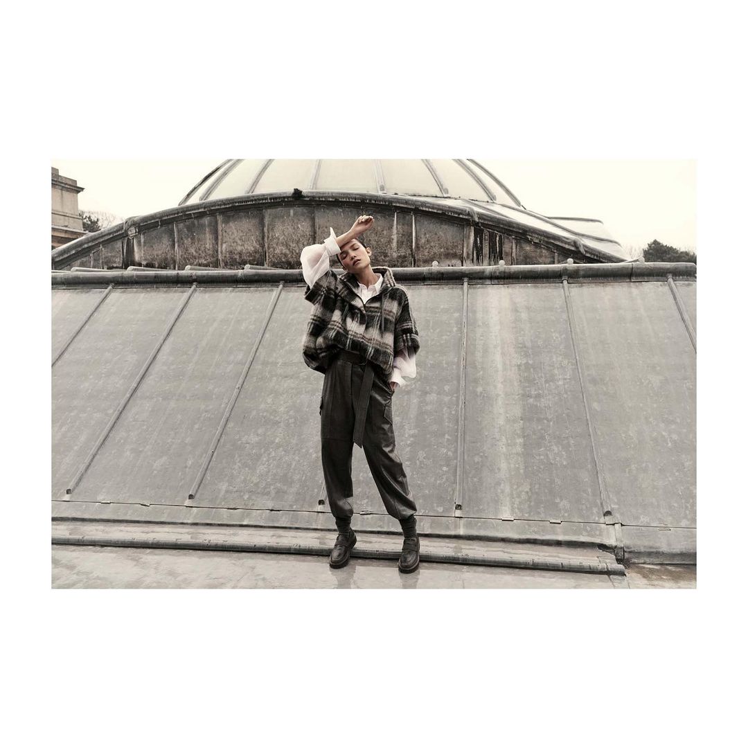 A person in a flannel jacket and pants poses on a rooftop with a large dome in the background, creating a fashion editorial image.