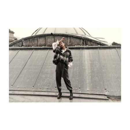 A person in a flannel jacket and pants poses on a rooftop with a large dome in the background, creating a fashion editorial image.