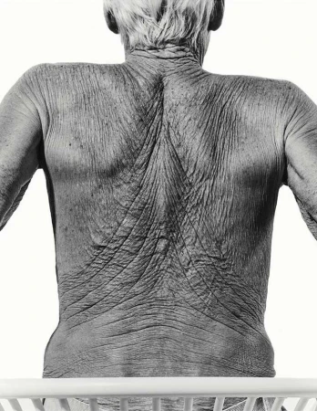 Monochrome close-up of an elderly person's wrinkled back and shoulders, showcasing skin texture against a bright background.