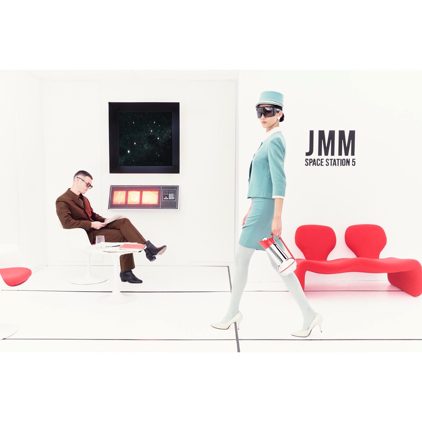 Fashionable woman in a light blue skirt suit walks past a man reading in a futuristic white waiting room with red bench seating.