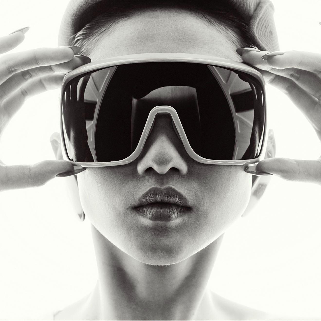 Monochrome portrait of a stylish woman with short hair, wearing oversized sunglasses and holding the frame with manicured fingers.
