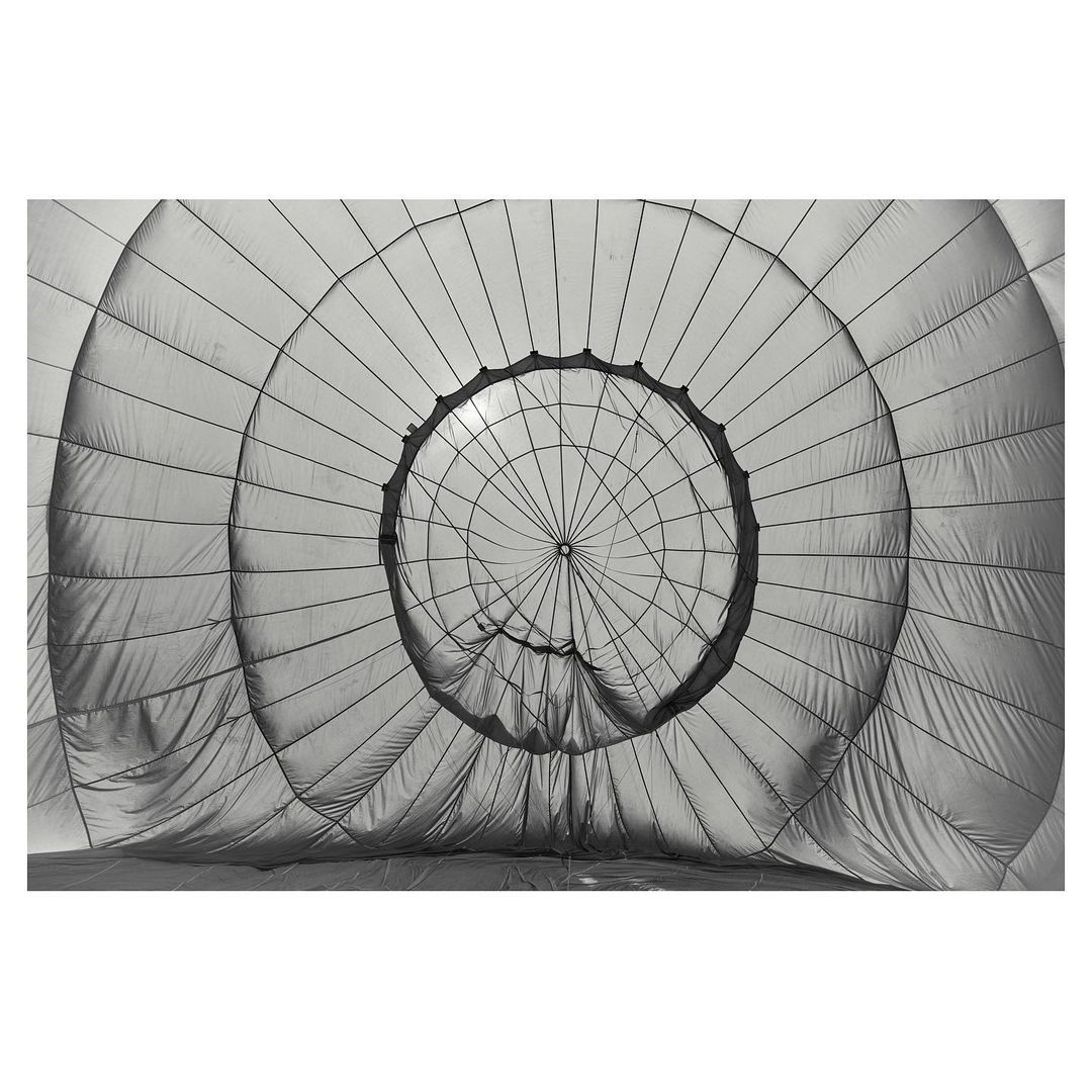 Inside a hot air balloon, creating an abstract, monochrome scene with lines converging towards a central light source and fabric textures.