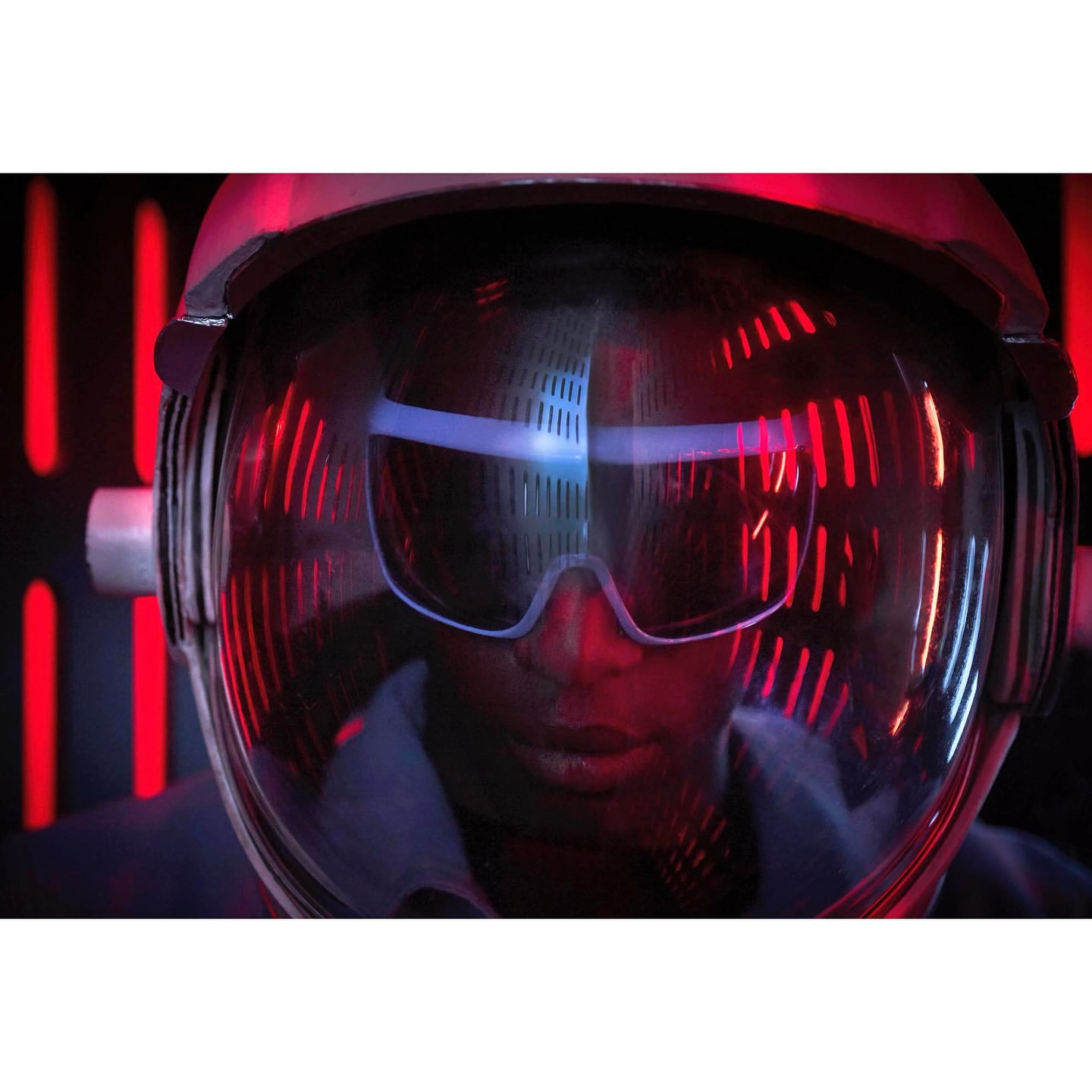 Close-up of an adult wearing a reflective astronaut helmet with visor and red LED lighting in the background in a studio setting.